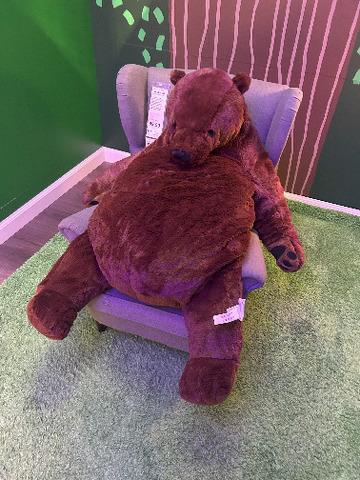Image of a large brown bear stuffed animal sitting on a purple chair.